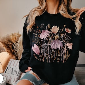 May include: Black sweatshirt with a watercolor floral print featuring pink, purple, and brown flowers on a black background.