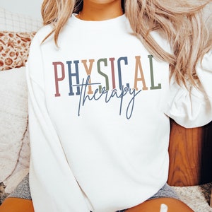 May include: White sweatshirt with the text "PHYSICAL therapy" in colorful letters.