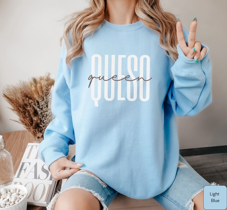 May include: Light blue sweatshirt with the text "QUESO queen" in white lettering.