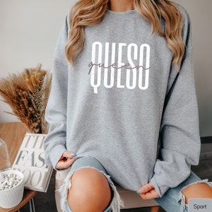 May include: A gray sweatshirt with the text "QUESO queen" printed in white on the front. The sweatshirt is being worn by a person with long blonde hair.