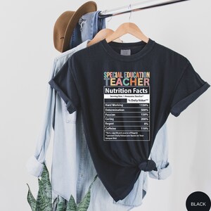 Op de afbeelding: Zwart T-shirt met een afbeelding van een voedingswaarde-etiket voor een "leraar speciaal onderwijs". Het etiket geeft het percentage van de dagelijkse waarde voor hard werken, vastberadenheid, passie, zorgzaamheid, spijt en cafe&iuml;ne.