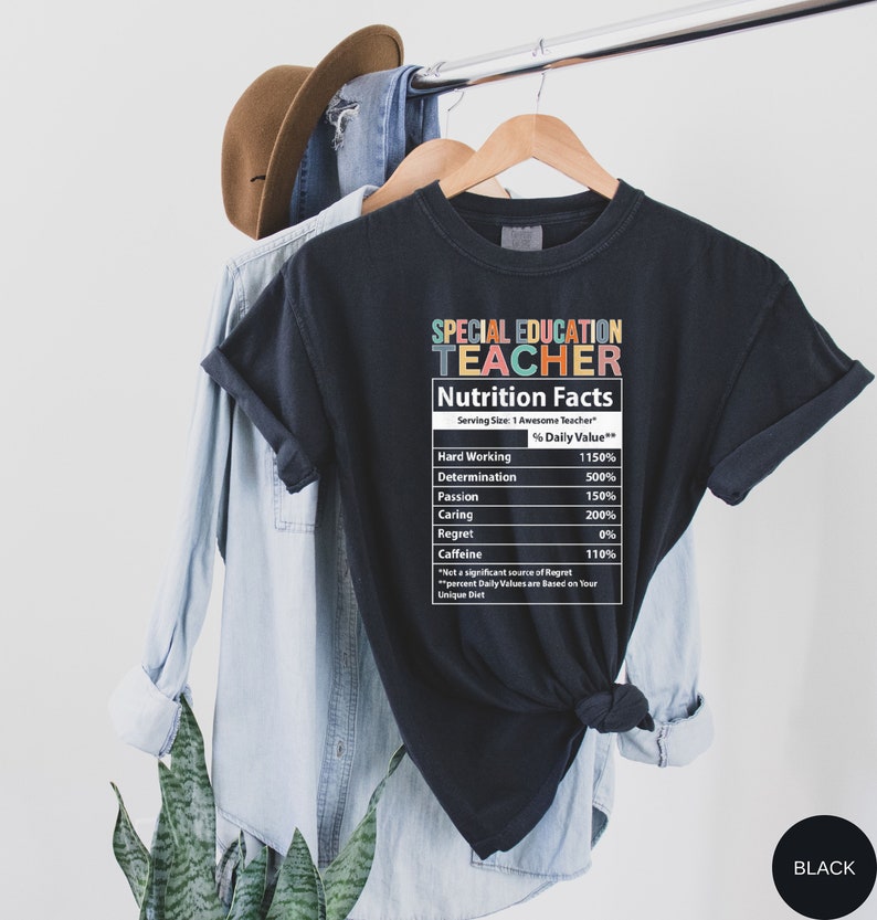 Op de afbeelding: Zwart T-shirt met een afbeelding van een voedingswaarde-etiket voor een "leraar speciaal onderwijs". Het etiket geeft het percentage van de dagelijkse waarde voor hard werken, vastberadenheid, passie, zorgzaamheid, spijt en cafe&iuml;ne.