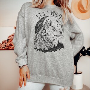 May include: A gray sweatshirt with a black wolf design and the text "Stay Wild" printed on the front.