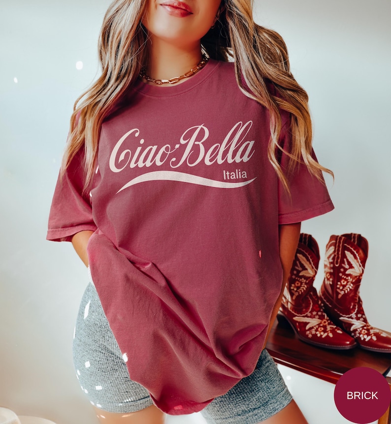 A model wears a brick shirt that says ciao-bella is a classic script style. It has a wavy ribbon underneath and says Italia.