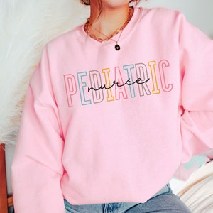 May include: A light pink sweatshirt with the text "PEDIATRIC nurse" in colorful letters.