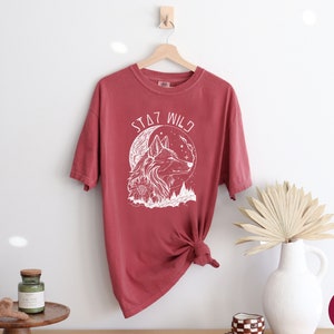 May include: A red t-shirt with a white wolf graphic and the text "Stay Wild".