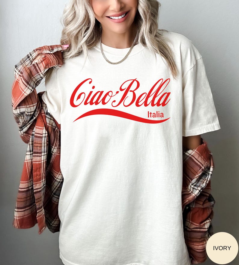 A model wears an ivory shirt that says ciao-bella is a classic script style. It has a wavy ribbon underneath and says Italia.