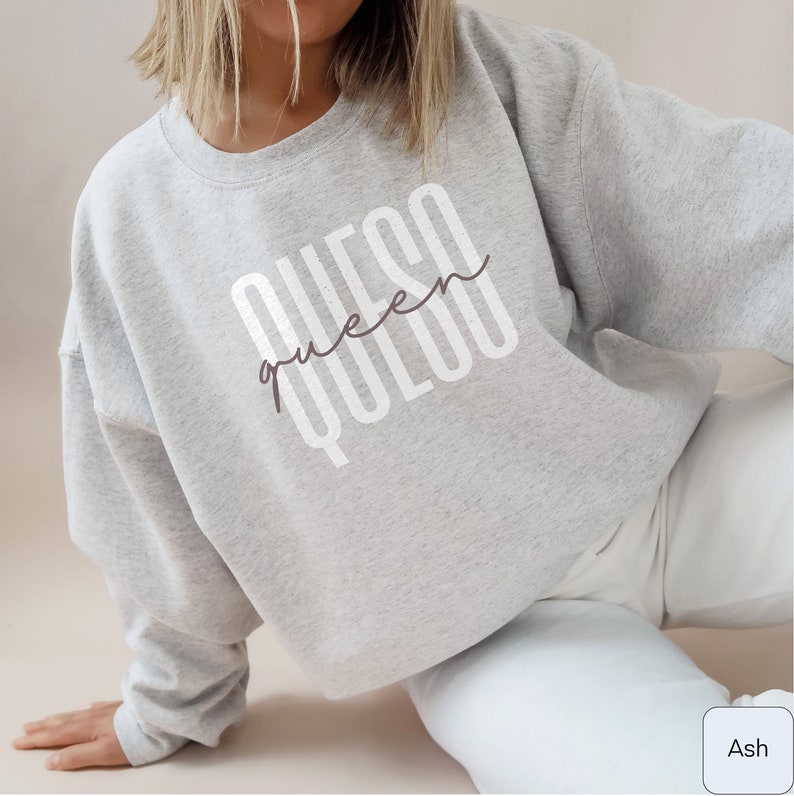 May include: A gray sweatshirt with the text "QUESO queen QUESO" printed on the front in white. The text is in a stylized font with the word "queen" written in cursive.
