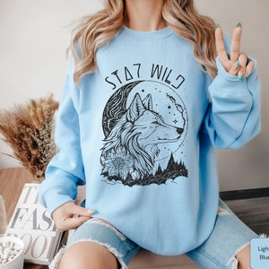May include: Light blue sweatshirt with a black wolf and moon graphic and the text "Stay Wild".