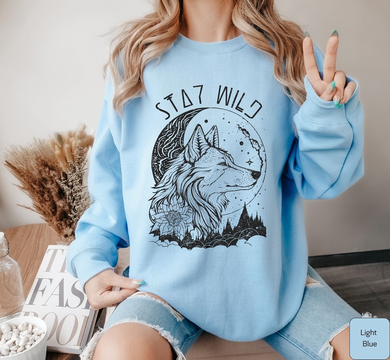 May include: Light blue sweatshirt with a black wolf and moon graphic and the text "Stay Wild".