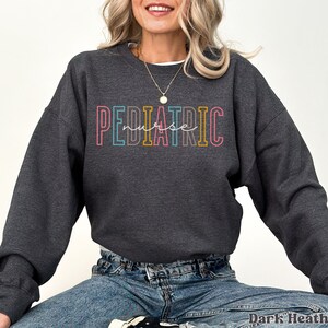 May include: Dark heather grey sweatshirt with the text "PEDIATRIC nurse" in rainbow colors.