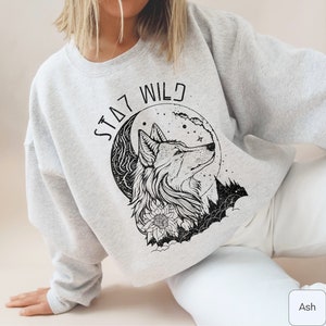 May include: A gray sweatshirt with a black and white graphic print of a wolf howling at the moon. The text "STAY WILD" is printed above the wolf.