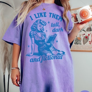 A model wears a violet shirt that has a retro design all in medium blue that days I like them tall, dark and fictional, with a woman from the 1950s sittings and reading a book.