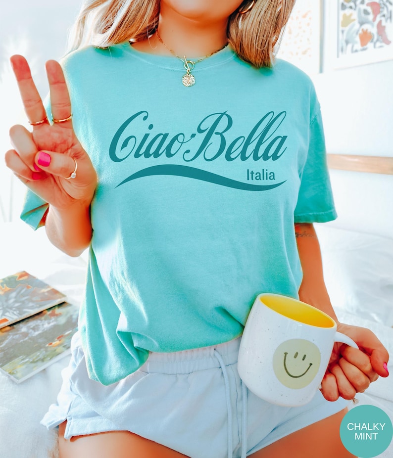 A model wears a chalky mint shirt that says ciao-bella is a classic script style. It has a wavy ribbon underneath and says Italia.