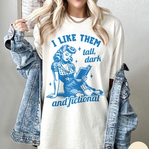 A model wears an ivory shirt that has a retro design all in medium blue that days I like them tall, dark and fictional, with a woman from the 1950s sittings and reading a book.