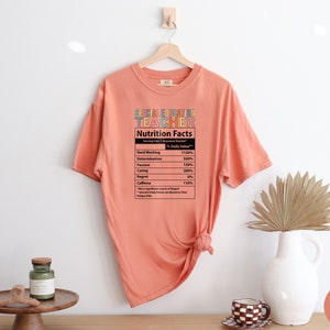 Op de afbeelding: Een perzikkleurig T-shirt met een afbeelding met de tekst "Special Education Teacher" en een voedingsschema met de vermelding "Hard Working 1150%, Determination 500%, Passion 150%, Caring 200%, Regret 0%, Caffeine 110%".