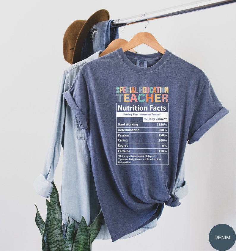 Op de afbeelding: Een blauw t-shirt met een afbeelding van een voedingsschema voor een "leraar voor speciaal onderwijs". Het schema geeft het percentage dagelijkse waarde voor hard werken, vastberadenheid, passie, zorg, spijt en cafe&iuml;ne.