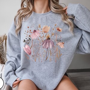 May include: A gray sweatshirt with a floral print featuring pink, brown, and white flowers. The sweatshirt has a crew neck and long sleeves.