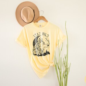 May include: A yellow t-shirt with a black wolf graphic and the text "Stay Wild".