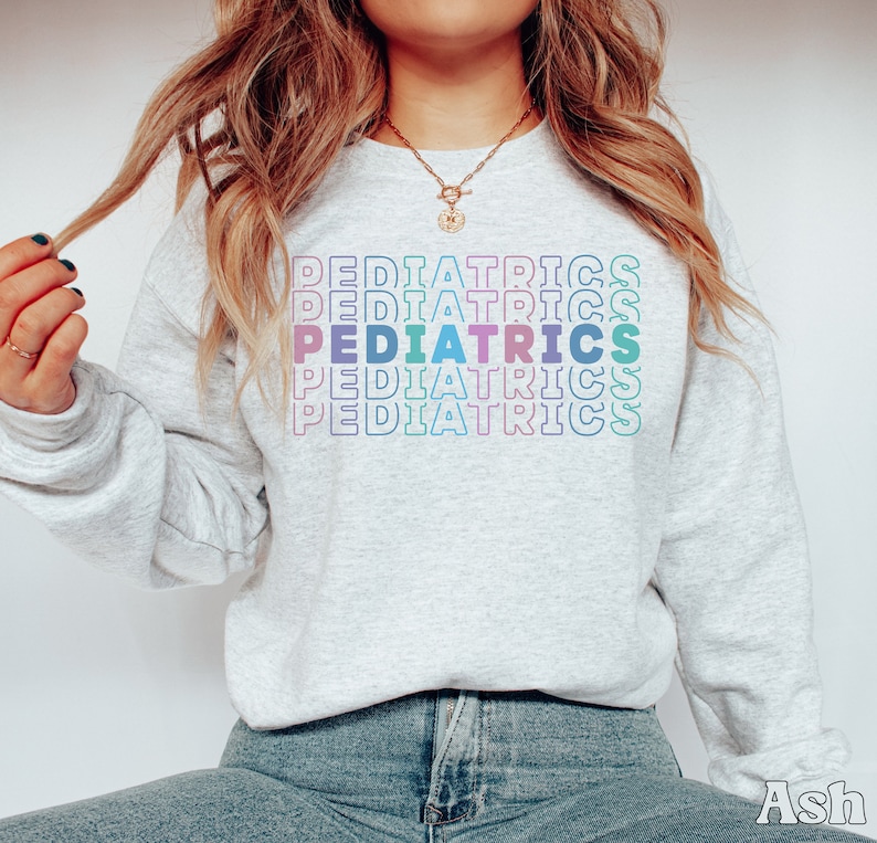 K&ouml;nnte beinhalten: Ein graues Sweatshirt mit dem Wort "PEDIATRICS", das in Regenbogenfarben wiederholt wird.