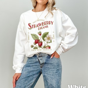 May include: White sweatshirt with a graphic print of strawberries and the text "FRUITY GOODNESS STRAWBERRY DREAMS SWEET JUICY FARM FRESH DELICIOUS".
