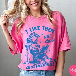 A model wears a crunchberry shirt that has a retro design all in medium blue that days I like them tall, dark and fictional, with a woman from the 1950s sittings and reading a book.