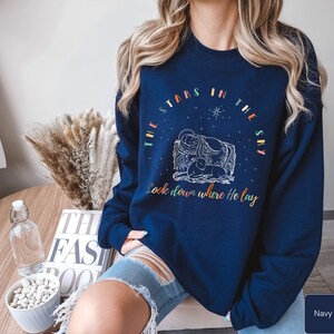May include: Navy blue sweatshirt with a white graphic of the nativity scene and the text "The stars in the sky look down where He lay".