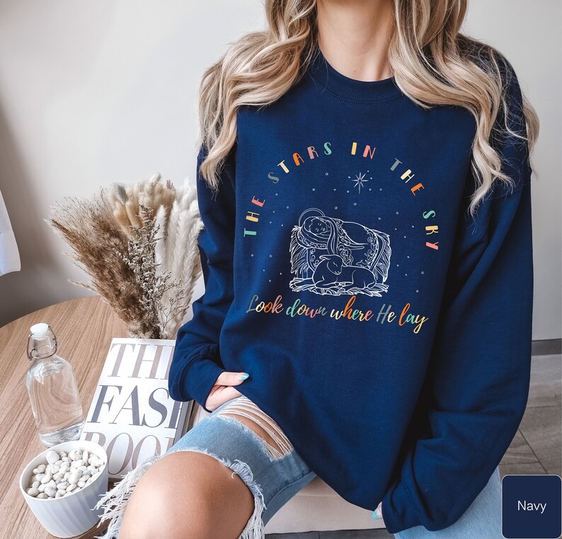 May include: Navy blue sweatshirt with a white graphic of the nativity scene and the text "The stars in the sky look down where He lay".