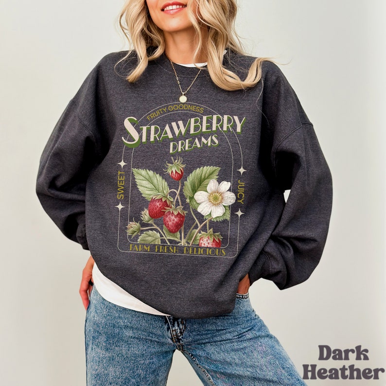 May include: Dark heather grey sweatshirt with a graphic print of a strawberry plant with the text "FRUITY GOODNESS STRAWBERRY DREAMS SWEET JUICY FARM FRESH DELICIOUS"