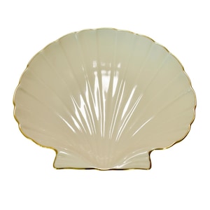 May include: A cream-colored, shell-shaped decorative dish with a gold-colored trim. The dish has a ribbed design radiating from the center, creating a fan-like pattern. The edges are scalloped, adding to the shell's aesthetic.