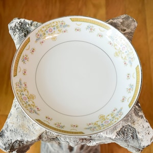 May include: A white ceramic bowl with a gold rim and floral pattern. The bowl has a delicate floral design in shades of pink, yellow, and green.