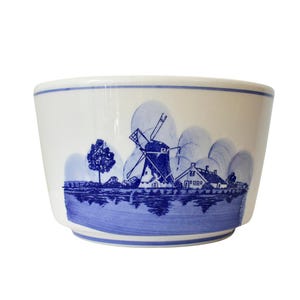 May include: White ceramic bowl with a blue Dutch windmill and landscape design. The bowl features a blue and white color scheme, with a detailed illustration of a windmill, trees, and houses. The bowl has a rounded shape.