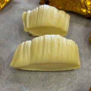May include: Two white chocolate candies, shaped like a half-moon, with a rippled texture. The candies are on a white parchment paper surface.