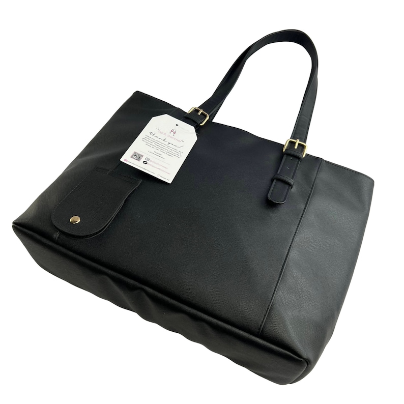 Peut inclure: Sac cabas noir avec une boucle dor&eacute;e et une petite poche sur le devant. Le sac a une &eacute;tiquette attach&eacute;e qui dit "Merci !"