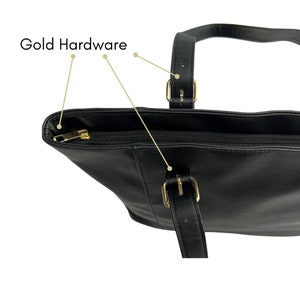 Peut inclure: Sac cabas noir avec des ferrures dor&eacute;es et une fermeture &agrave; glissi&egrave;re. Le sac a deux poign&eacute;es sup&eacute;rieures avec des boucles dor&eacute;es.
