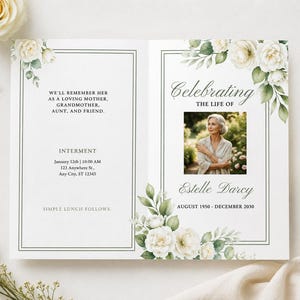 Può includere: Un modello di programma funebre con rose bianche e foglie verdi. Il testo recita: Celebrating the life of Estelle Darcy, August 1950 - December 2030, con la foto di una persona e i dettagli per la sepoltura il 12 gennaio alle ore 10:00.