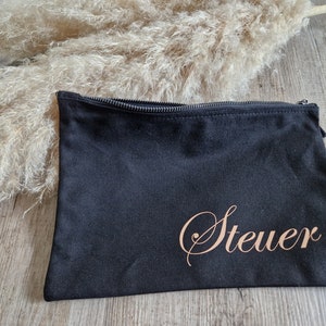 Könnte beinhalten: Schwarze Kosmetiktasche mit Reißverschluss und dem Namen "Steuer" in roségoldener Schrift.