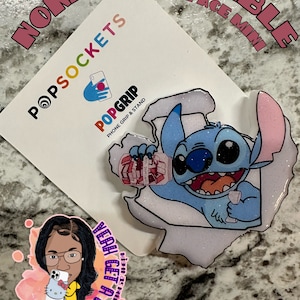 May include: A blue and white Stitch character phone grip with glitter accents. The phone grip is attached to a white background with the words "PopGrip" and "Phone Grip & Stand" printed on it. The background also has the words "None Swappable Ghostface Mini PopSockets" printed on it.