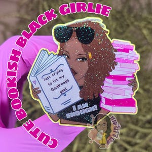 May include: A glittery sticker featuring a Black woman with sunglasses, holding a book and a stack of pink books. The book reads "Just trying to hit my Goodreads goal." Text around the image says "Bookish Black Girlie" and "Cute."