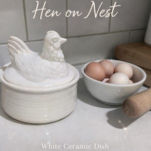 May include: A white ceramic mug with a black handle and the text "But First, Coffee" in a bold, black font. The mug is set against a blurred background, highlighting its clean design.