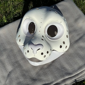 Op de afbeelding: Witte, onafgewerkte harige dierenmasker met gaten voor ogen en neus. Het masker is gemaakt van hard plastic materiaal en heeft een witte achtergrond.