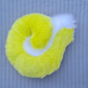 May include: A fluffy, yellow and white tail prop, possibly for a costume. The tail is a bright yellow with a white swirl and tip. The tail is made of soft, fluffy material.