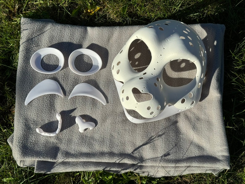 Op de afbeelding: Witte, onafgewerkte harige masker met aparte witte kunststof ogen, neus, tanden en wenkbrauwen. Het masker is gemaakt voor een harige kostuum.
