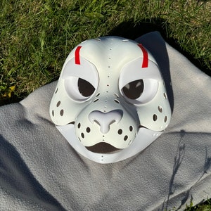 Op de afbeelding: Witte harige dierenmasker met rode accenten en zwarte ooggaten. Het masker heeft een witte neus en een witte mond.
