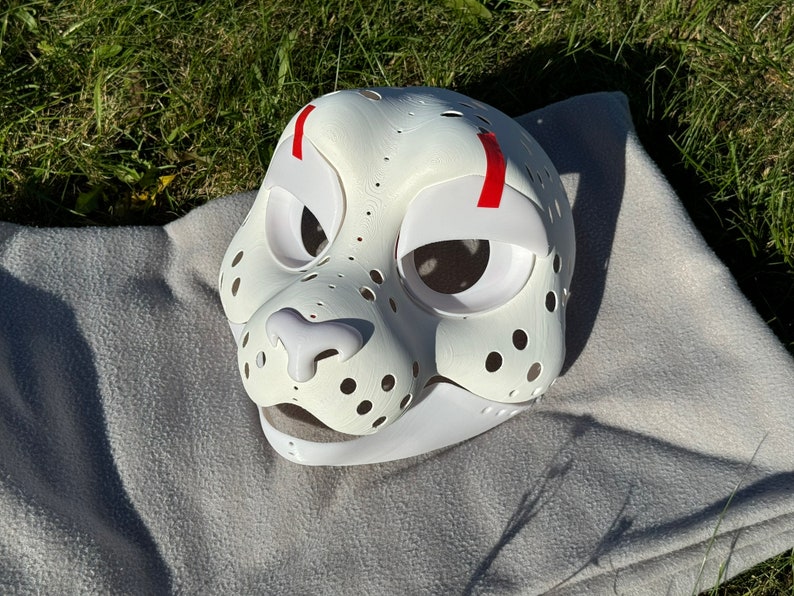 Op de afbeelding: Witte, onafgewerkte vachtdiermasker met rode markeringen rond de ogen. Het masker heeft een gedetailleerd neus- en mondgebied met gaten voor ventilatie.