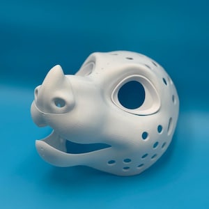 Könnte beinhalten: Eine weiße, 3D-gedruckte Tiermaske mit einer markanten Schnauze, einem kleinen Horn auf dem Nasenrücken und großen Augenhöhlen. Die Oberfläche der Maske ist mit zahlreichen kleinen, kreisförmigen Belüftungslöchern an den Seiten und oben versehen.