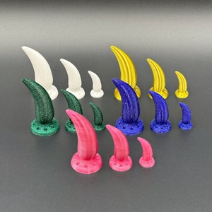 Op de afbeelding: Een set van 12 kleurrijke plastic hoorns, elk met een andere kleur en maat. De hoorns zijn in een halve cirkel op een grijs oppervlak gerangschikt.