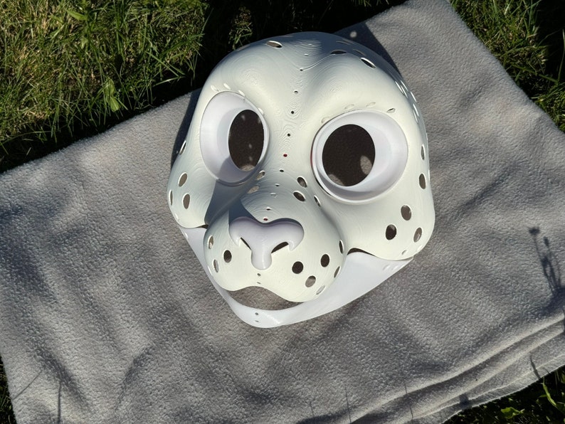 Op de afbeelding: Witte, onafgewerkte harige dierenmasker met gaten voor ogen en neus. Het masker is gemaakt van hard plastic materiaal en heeft een witte achtergrond.