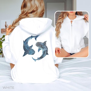Puede incluir: Sudadera con capucha blanca con un diseño de tiburón ballena azul y blanco en la espalda. La sudadera tiene una cremallera y una capucha.