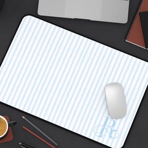 May include: A rectangular desk mat featuring a light blue and white vertical striped pattern with a large, decorative letter R monogram in the bottom right corner. The mat has a solid black border and a smooth surface finish for computer mouse use.